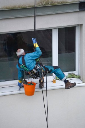 Foto de Toulouse, Francia - 19 de febrero de 2024 - rappel industrial: un trabajador experimentado suspendido de un cable, equipado con un arnés, limpia ventanas de vidrio en un edificio residencial de gran altura y varios pisos - Imagen libre de derechos
