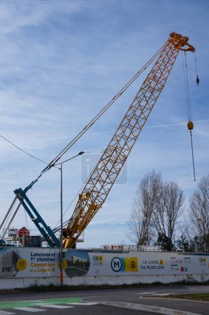Photo for Labge, France - Feb. 18, 2024 - Behind a construction barrier that also serves as an information board about the extension of Toulouse's Metro Line B, a crawler crane with a yellow steel boom - Royalty Free Image