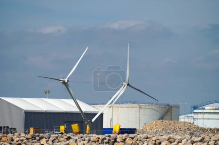 Photo for Port-la-Nouvelle, France - April 5, 2024 - Off-shore floating wind turbines under assembly on the docks of Port-la-Nouvelle commercial harbor; in the background, circular tanks in an oil storage - Royalty Free Image