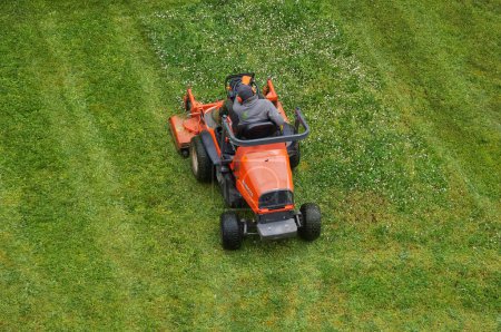 Photo for Toulouse, France - April 18, 2024 - Top view above a gardener with ear protection, in action at work on an orange, Japanese Kubota riding mower, maintaining the lawn on a university campus in Rangueil - Royalty Free Image