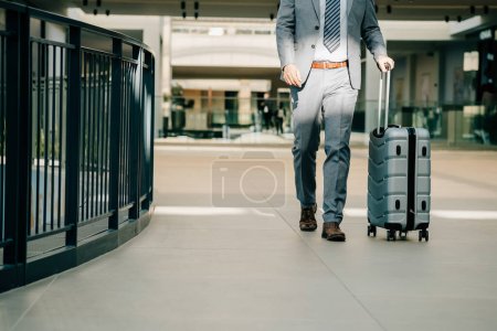 Téléchargez les photos : Fermer Photo des jambes d'homme d'affaires marchant avec des bagages à l'aéroport - en image libre de droit