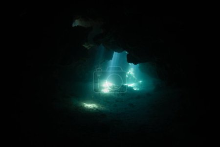 Foto de Rayos de luz solar descienden a través de agujeros en un arrecife de coral hacia una caverna sumergida en Fiji. Los arrecifes a menudo se erosionan en grietas estrechas, cañones y cuevas.. - Imagen libre de derechos