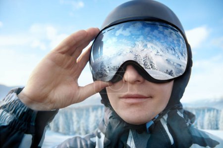 Photo for Close Up Of The Ski Goggles Of A Man With The Reflection Of Snowed Mountains. Man On The Background Blue Sky. Wearing Ski Glasses. Winter Sports - Royalty Free Image