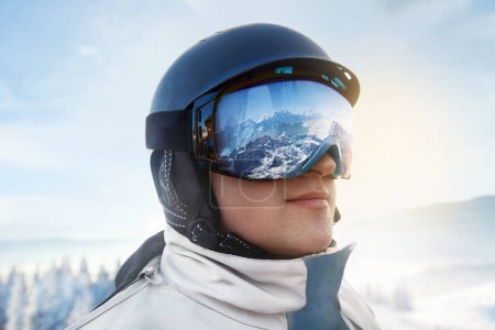 Photo for Close Up Of The Ski Goggles Of A Man With The Reflection Of Snowed Mountains. Man In The Background Blue Sky.  Winter Sports - Royalty Free Image
