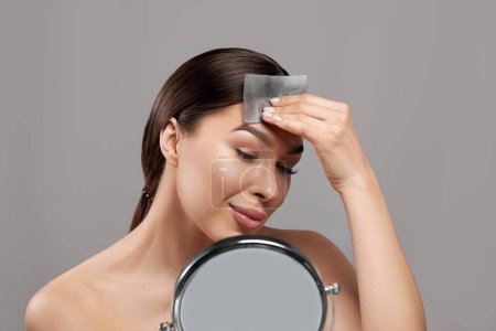 Téléchargez les photos : Beautiful woman using facial oil blotting paper.  Cosmetology, cosmetics. Facial treatment - en image libre de droit
