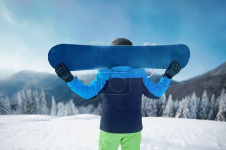 Photo for Snowboarder Of Man At Ski Resort On Blue Sky and Snow Mountains Background, Hold Snowboard. Winter Sports - Royalty Free Image
