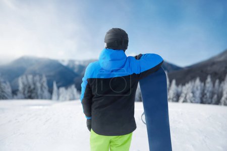 Photo for Snowboarder Of Man At Ski Resort On Blue Sky and Snow Mountains Background, Hold Snowboard. Winter Sports - Royalty Free Image