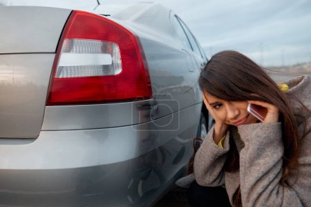 Téléchargez les photos : Femme triste debout près de la voiture avec des rayures sur le parking et parler au téléphone
. - en image libre de droit