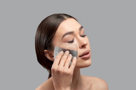 Belle femme séduisante utilisant un film propre à l'huile faciale pour enlever l'huile sur le visage pour la peau fraîche du visage si fraîche et propre, Concept de beauté, Isolé sur fond gris
