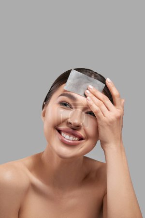 Photo for Face skin care. Smiling woman using facial oil blotting paper portrait. Closeup of beautiful happy girl model with natural makeup using oil absorbing sheets, beauty product - Royalty Free Image