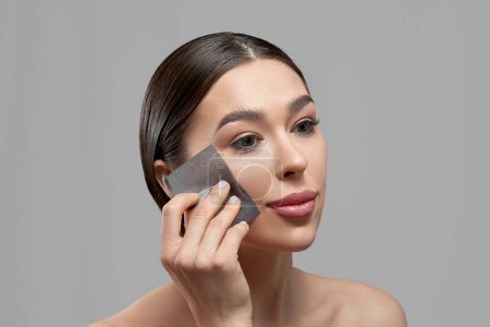 Téléchargez les photos : Beautiful woman using facial oil blotting paper.  Beauty concept. Cosmetology, cosmetics. Facial treatment - en image libre de droit