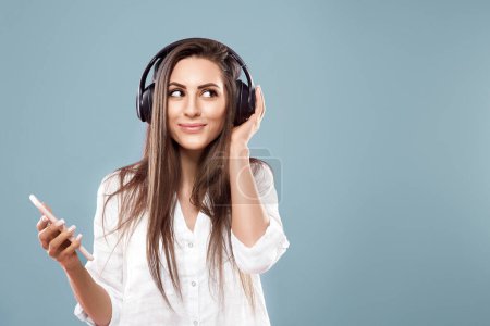 Belle femme écoutant de la musique à l'aide d'écouteurs sans fil dans le studio isolé sur fond bleu.
