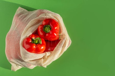 Foto de Pimientos dulces rojos en una bolsa de compras sobre un fondo verde. flatlay. copia de espacio a la derecha - Imagen libre de derechos