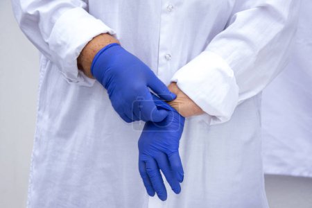 Photo for The hands of a doctor in latex gloves. The doctor puts on sterile gloves against the background of a medical gown. Infection control concept. - Royalty Free Image