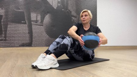 Die Frau macht Bauchübungen mit einem fitten Ball. Fitnesstraining in Innenräumen mit Geräten für Kraftaufbau und Beweglichkeit.