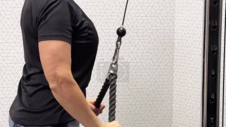 Una persona en un gimnasio, con una camiseta negra, está tirando de una máquina de cable para el entrenamiento de resistencia. Concepto: Entrenamiento de fitness en interiores. Vídeo horizontal.
