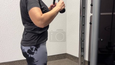 Hand work on the simulator, close-up video. Triceps extension down on a block. A person is using a gym machine, focusing on their workout. The modern interior of the fitness center is visible. Concept