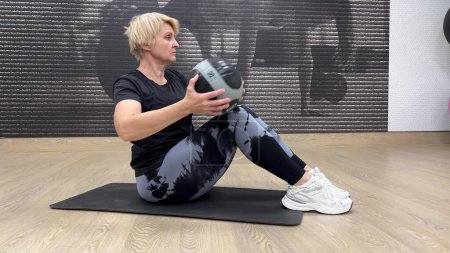 Video de una mujer gorda de 55-60 años entrenando en el gimnasio con una pelota. La mujer en el gimnasio realiza ejercicios abdominales con una pelota en forma. Concepto: Un momento que captura un entrenamiento físico intenso que involucra