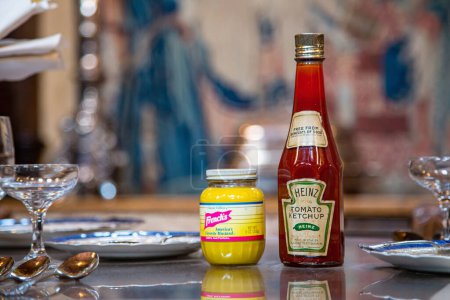 Foto de Hearst Castle, California, Estados Unidos - 27 de abril de 2017- Botella vintage de ketchup Heinz y mostaza francesa sentada en una mesa de juego en el refectorio de Hearst Castle, sobre un tapiz borroso. - Imagen libre de derechos