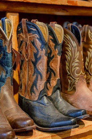 Cowboy boots in a store. Close-up of new cowboy boots on shelf. Aligned cowboys boots on a shelf in a store. Ostrich leather cowboy boots lined up in a row in a retail store. Vertical photo