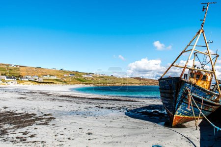 Photo for Abandoned boat or fishing trawler on Arranmore island, Republic of Ireland. The sun is shining on a rusty vessel stranded in Aphort Strand, County Donegal. Forsaken slanting ship on Irish white beach - County Donegal, Republic of Ireland - Royalty Free Image