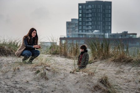 Téléchargez les photos : Mère appréhendée parlant avec son enfant sur une plage de la ville. Un gamin qui écoute sa mère parler. Maman et son fils discutent en plein air montrent combien la conversation est importante pour une relation familiale sereine - Amager, Copenhague, Danemark - en image libre de droit