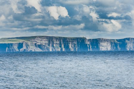 Foto de Cliffs of Moher front view from the sea. Big clouds hovering the high cliffs of Moher in west Ireland, County - Co Clare, picturing a dramatic Atlantic seascape with rock layers visible from Inisheer, Aran Islands. Ireland - Imagen libre de derechos