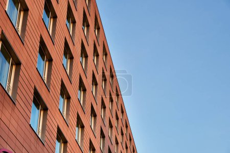 Foto de Moderna fachada de ladrillo naranja con ventanas contra el cielo es un ejemplo de la construcción de una arquitectura ordenada. Exterior moderno construido con grandes ladrillos naranja muestra estilo de vida contemporáneo, apartamentos modernos - Imagen libre de derechos