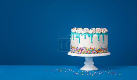 Téléchargez les photos : Gâteau goutte à goutte d'anniversaire blanc avec ganache sarcelle et saupoudrer coloré sur un fond bleu foncé. Simple et tendance. Espace de copie. - en image libre de droit