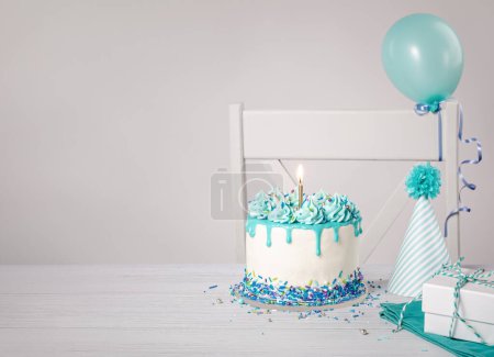 Photo for Blue and white birthday party with a buttercream drip cake, sprinkles, bright gold candle, hat and balloons on a light grey background. Trendy. Copy space. - Royalty Free Image