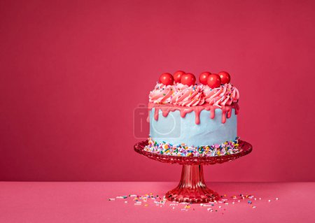 Photo for Bubble gum Birthday Drip Cake on a red stand with colorful sprinkles, buttercream icing and red cherry candy balls on a vibrant pink background. Over the top fun. Copy space. - Royalty Free Image