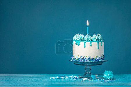 Foto de Pastel de goteo blanco con ganache de teca, salpicaduras y una vela encendida sobre un fondo azul. Simple y de moda. Copiar espacio. - Imagen libre de derechos