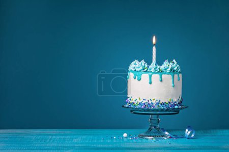 Weißer Tropfkuchen mit Krickenten-Ganache, Streusel und einer brennenden Geburtstagskerze vor blauem Hintergrund. Einfach und trendy. Kopierraum.