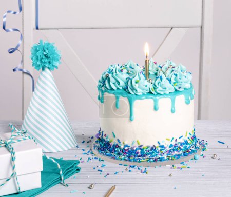 Foto de Fiesta de cumpleaños azul y blanca con pastel de goteo, espolvoreos, velas y divertido sombrero sobre un fondo blanco. - Imagen libre de derechos