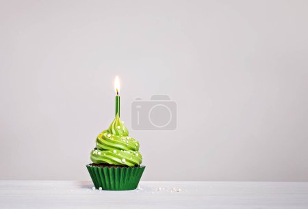 Photo for Green birthday cupcake with buttercream icing, sprinkles and lit candle on a light grey white background. copy space. - Royalty Free Image