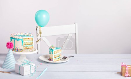 Photo for Birthday party table setting with a teal blue ganache drip cake on a light grey white background with sliced piece of cake and decorations. Copy space. - Royalty Free Image