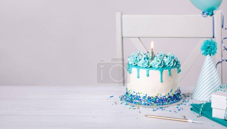 Photo for Blue and white birthday party with drip cake, sprinkles, candle, hat and balloons on a white background. Copy space. - Royalty Free Image