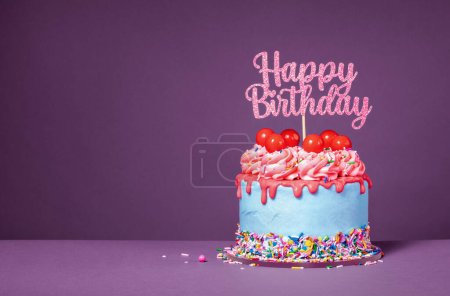 Lustiger Tropfkuchen mit roter Ganache, Gummibällchen, Streuseln und einem Happy Birthday Topper vor lila Hintergrund. Kopierraum.