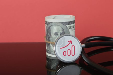 Téléchargez les photos : Billets d'argent et stéthoscope avec symbole d'augmentation des coûts des soins de santé. - en image libre de droit