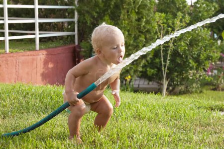 Téléchargez les photos : Child toddler boy playing with water hose outdoors in summer, summer activities . High quality photo - en image libre de droit
