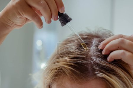 Foto de La mujer se aplica aceite en el cabello con pipeta. Belleza cuidado del cuero cabelludo y el cabello - Imagen libre de derechos
