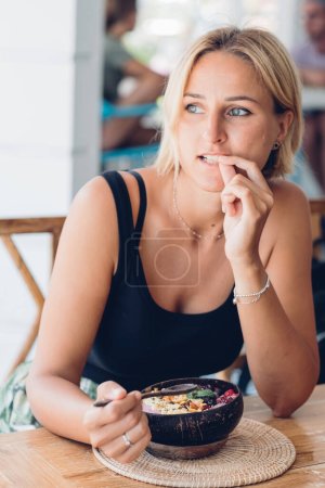 Foto de Mujer comiendo batido de bayas con semillas de frutas y granola de la taza de coco. Alimentación saludable y concepto de cero residuos. - Imagen libre de derechos