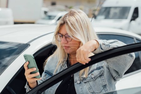 Foto de Mujer de pie cerca de coche y mirando su teléfono móvil, pagando por el aparcamiento y navega por la ciudad. - Imagen libre de derechos