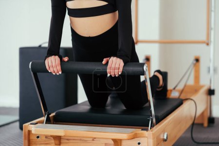 Foto de Mujer irreconocible usando ropa deportiva negra practicando ejercicios de pilates en la máquina reformadora en el estudio. - Imagen libre de derechos