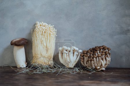 Foto de Various edible Asian mushrooms. Enoki, shimeji, shiitake, tea tree, royal oyster mushrooms. Set of vegetables. Dark photo natural light. - Imagen libre de derechos