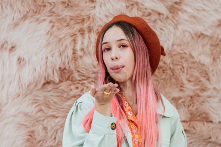 Photo for Stylish millennial teenager girl with color hair sends an air kiss. Portrait of a romantic young woman in a beret on a pink background. - Royalty Free Image
