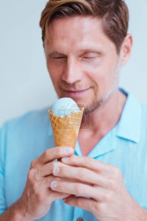 Foto de Retrato de cerca del hombre de mediana edad en camisa azul comiendo helado de lavanda de cono. - Imagen libre de derechos
