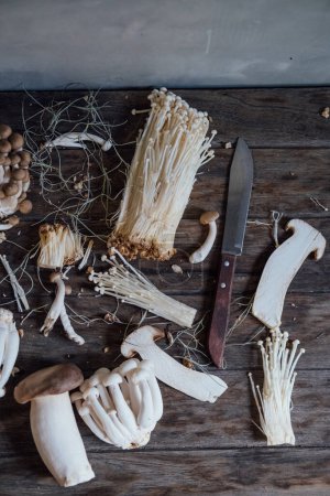 Foto de Various edible Asian mushrooms. Enoki, shimeji, shiitake, tea tree, royal oyster mushrooms. Set of vegetables. Dark photo natural light. Flatly. Selective focus. - Imagen libre de derechos