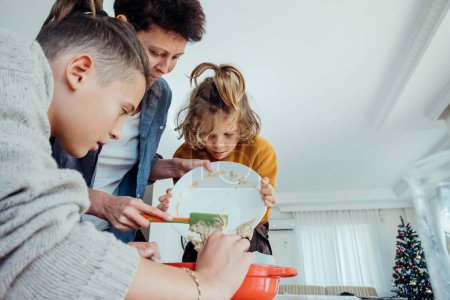 Foto de Madre con sus hijos niños haciendo galletas de Navidad en la cocina. Pasar tiempo juntos - Imagen libre de derechos