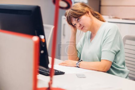 Foto de Mujer joven cansada sintiéndose aburrida sentada frente a la computadora en la oficina moderna - Imagen libre de derechos